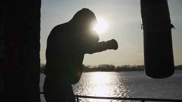 Boxer beats punching bag on sunset background. Silhouette motivation sport boxing. Epic video