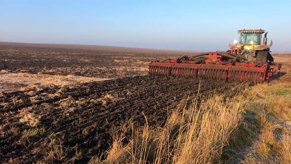 A Tractor Plows and Harrows the Land in a Large Field on a Sunny Spring Day