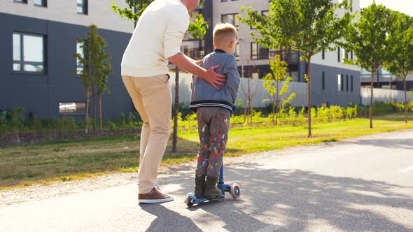 Happy Father and Son Riding Scooter in City