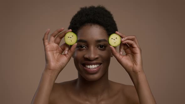 African Lady Posing With Cucumber Slices Covering Eyes Beige Background