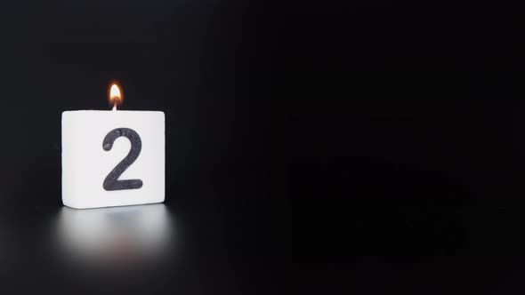 A square candle saying the number 2 being lit and blown out on a black background
