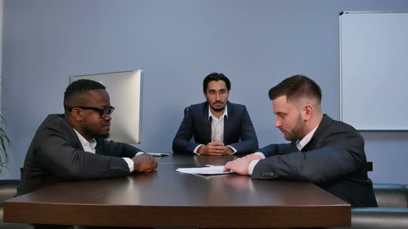 Young Serious Man Holding Papers, Reading Them Attentively, During Meeting in Office