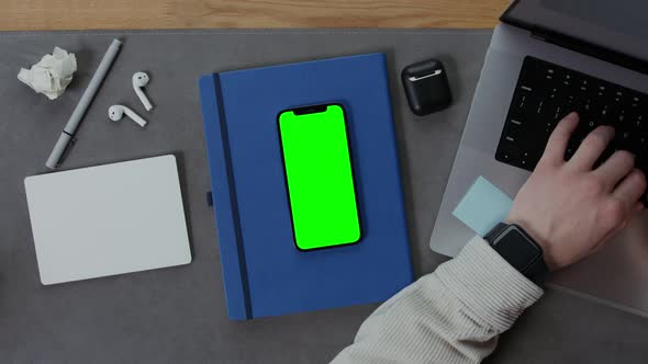 A Man is Typing on a Laptop at a Desktop with Mobile Phone Lying Next to It