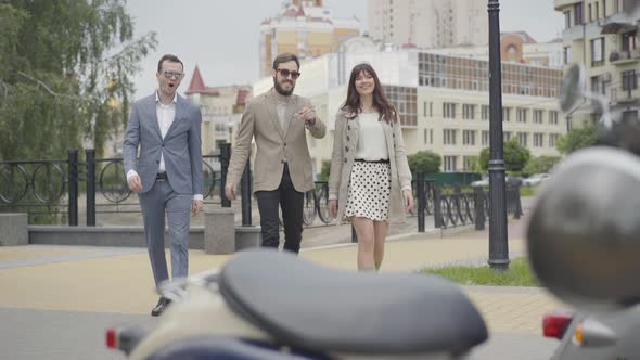 Portrait of Three Positive Male and Female Biker in Elegant Clothes Coming To Scooters Standing on