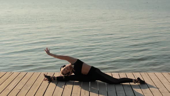 Woman Is Doing Longitudinal Split Sitting on Pier Near River and Tilting To Leg.