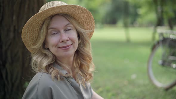 Closeup Portrait of Happy Smiling Middle Aged Woman in Straw Hat Enjoying Leisure in Summer Park