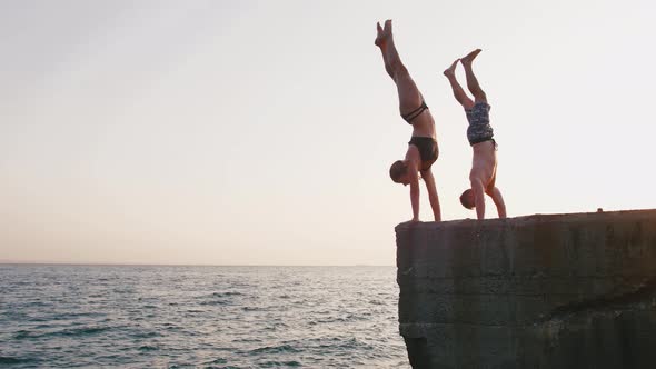 Young Woman and Man Jumping From a Pier Into the Sea and Doing Tricks During Beautiful Sunrise Slow