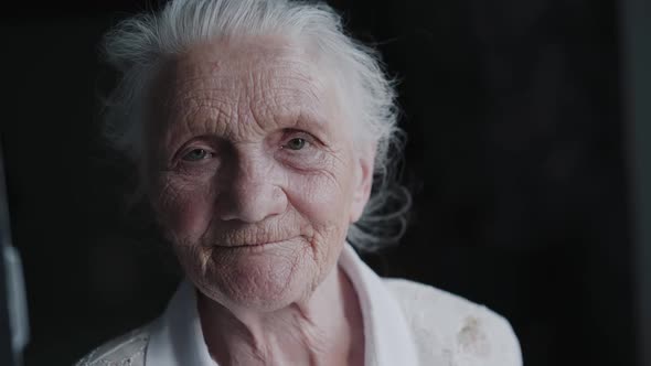 Portrait of Greyhaired Grandmother with Wrinkled Face Talks Easy Into Camera