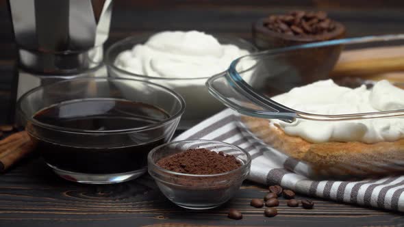 Italian Savoiardi Ladyfingers Biscuits and Cream in Baking Dish, Coffe Maker on Wooden Background