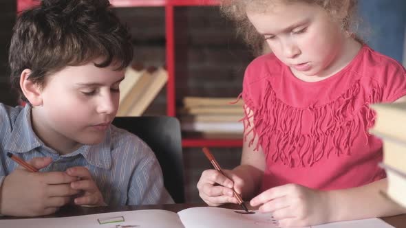 Cheerful children draw pictures with pencils and brushes on paper in the room.