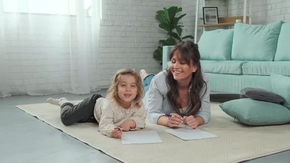Mom and Daughter Lying on Carpet on the Floor Drawing on Paper Together