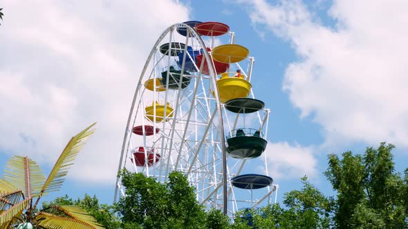 Large, Multi-colored Ferris Wheel Rotates Against a Blue and Slightly Cloudy Sky. Ferris Wheel in an