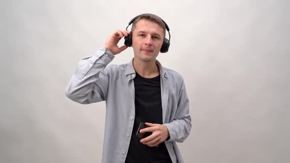 Young Man on a White Background in Headphones and a Smartphone Listens to Music and Dances