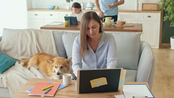 Busy Mom Working Remotely with Laptop Sitting on the Couch