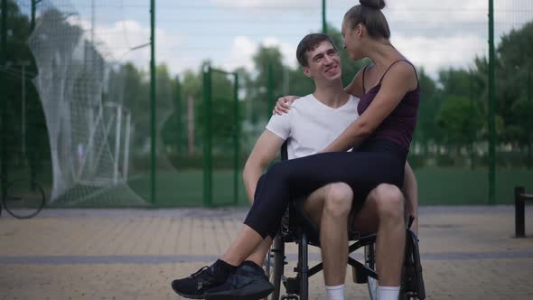 Front View Happy Caucasian Man in Wheelchair Rolling in Slow Motion As Smiling Woman Sitting on Lap