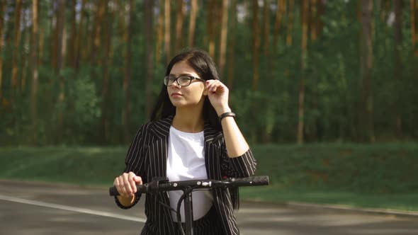 Young Business Woman Standing with Electric Scooter with Green Forest Background