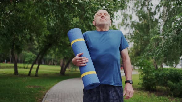 Handsome GrayHaired Old Man Standing in Park with Sport Mat and Looking in Camera