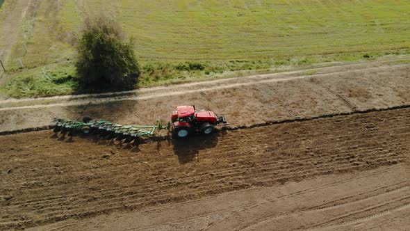 Aerial Shot of a Farmer on a Red Tractor Processing Farmland with a Reverse Plow with Support Wheels