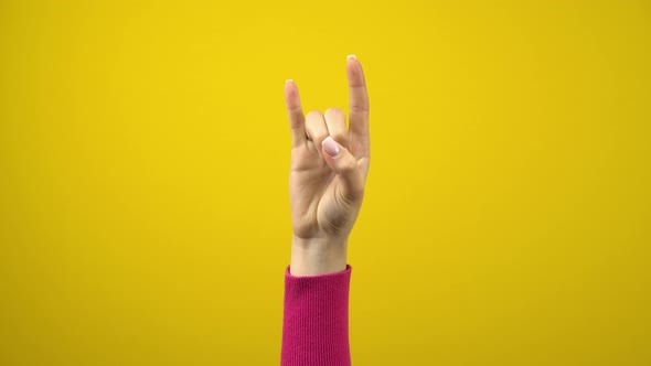 Female Hand Shows the Sign of the Horns. Studio Photography on an Isolated Yellow Background.