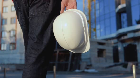 An Engineerarchitect in a White Shirt and Orange Work Vest Stands Against the Backdrop of a Modern