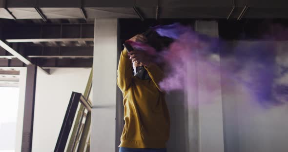 Mixed race woman holding blue and purple flares standing in an empty building