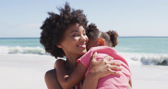 Smiling african american mother with daughter embracing on sunny beach