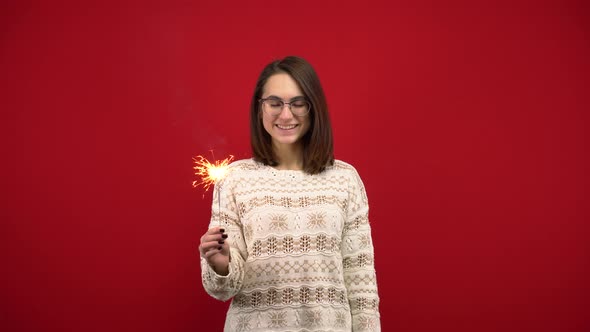 A Young Woman in a White Sweater Holds a Sparkler in Her Hand. Shooting in the Studio on a Red