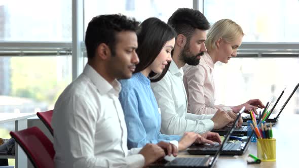 Four Office Clerks Closely Sitting and Working on Laptops.