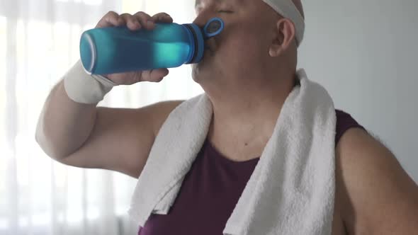 Thirsty obese person drinking water and relaxing after cardio training at home