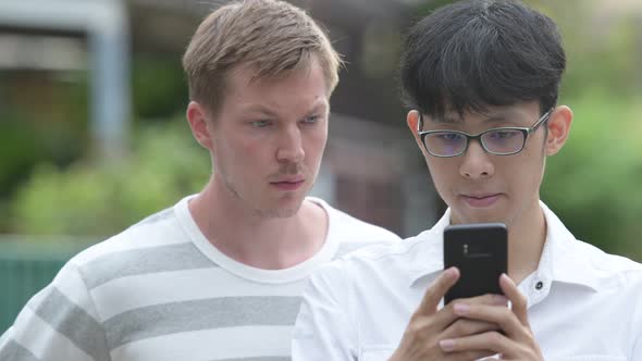 Two Multi-ethnic Businessmen Using Phone Together in the Streets Outdoors