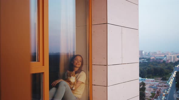 Smiling girl with a red cat by the window