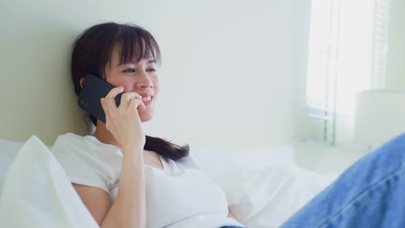 Asian attractive woman use mobile phone call while lying down on bed at home in morning.