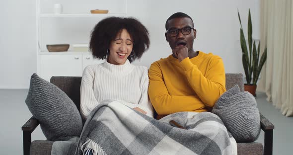 Curly Mixed Race Girl in White Sweater Sits Near Black Man with Glasses and Yellow Sweater Watching