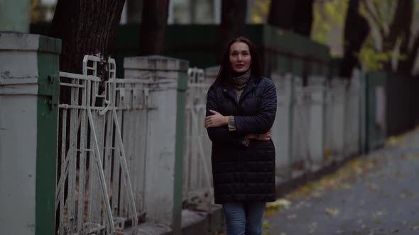 a Middle-aged Dark-haired Woman in a Black Jacket Walking a City Street on an Autumn Evening. Passes