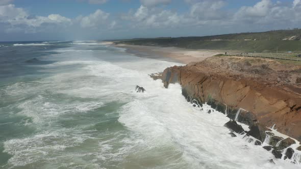 Aerial overview of waves slamming into cliff