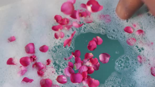 African american woman taking bath and touching flower petals in water in bathroom