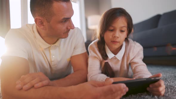 Father and Daughter Enjoying Time Together and Using a Tablet for Family Entertainment While Lying