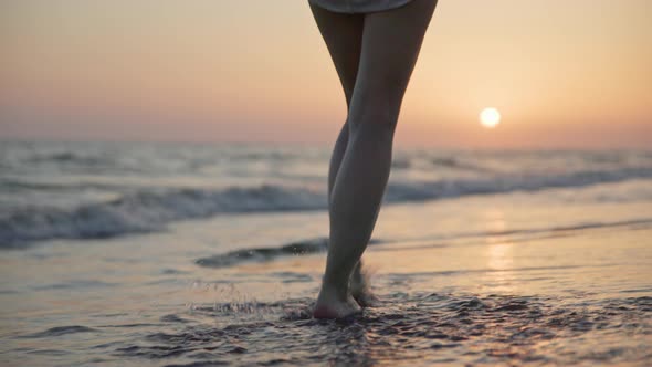 Beautiful female legs walking on the sea waves at sunset