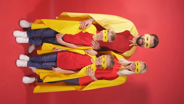 Family of Superheroes in Costumes Posing in Studio with Red Background.