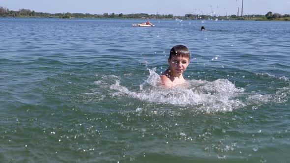 Happy Child Swimming Splashing on the Beach in Sunlight on Sea