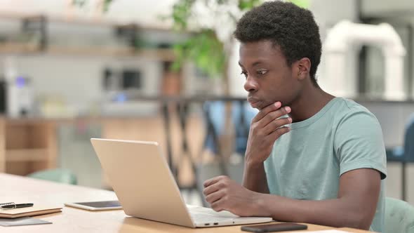 Pensive Young African Man Thinking and Working on Laptop