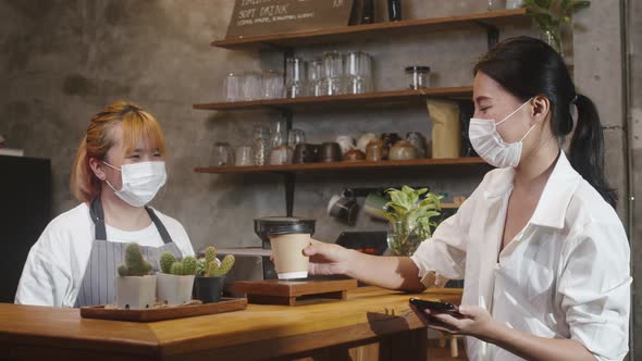 Young Asia female barista wear face mask serving take away hot coffee paper cup to consumer.