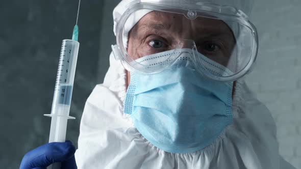 Doctor or Medical Lab Worker in Personal Chemical Protective Kit Holds a Syringe with Blue Liquid in