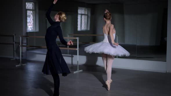 Two Slim Gorgeous Ballerinas in Black Dress and White Tutu Walking on Tiptoes in Dark Studio