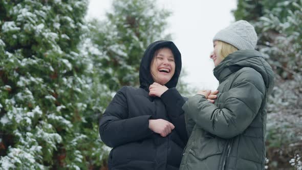Two Cheerful Female Friends Laughing Out Loud Standing Outdoors in Snowy Forest