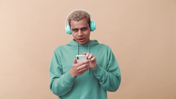 Cheerful curly-haired man wearing blue hoodie listening music in headphones