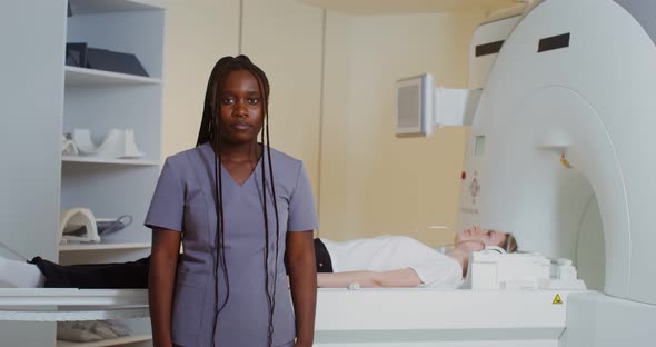 A Doctor Looks Into the Camera Standing in Front of an MRI Machine