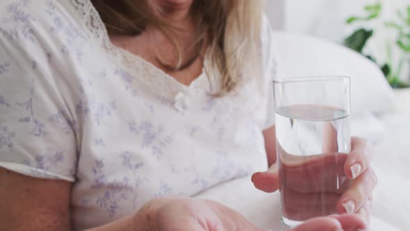 Senior woman holding pills and glass of water at home