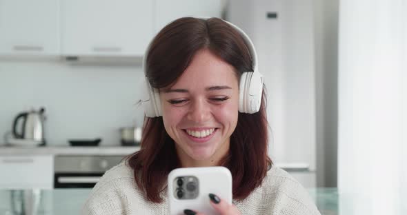 Attractive Brunette Woman is Talking to Someone with a Video Chat While Sitting in the White Cozy