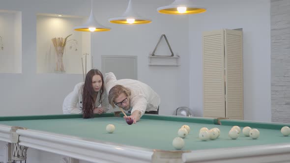 Successful Blond Bearded Man Teaches His Girlfriend To Play Billiard. Confident Man in White Shirt